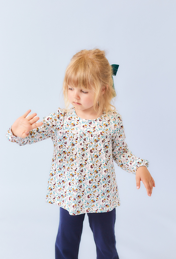 Biała bluzka dziewczęca z długim rękawem i kwiatowym nadrukiem.